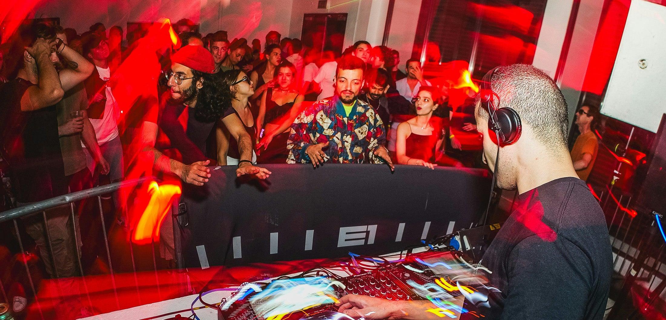 DJ mit roten EDM-Kopfhörern am Mixer vor tanzender Menge im Club – ideale Kopfhörer für Bassliebhaber 2025.