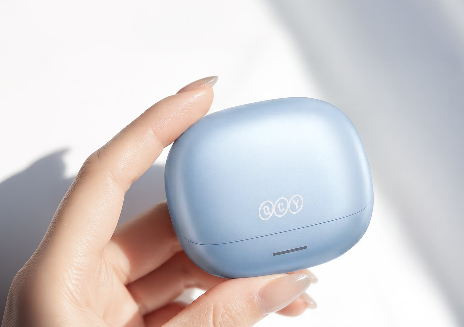 Auriculares Bluetooth QCY en azul claro, sostenidos en el estuche de carga.
