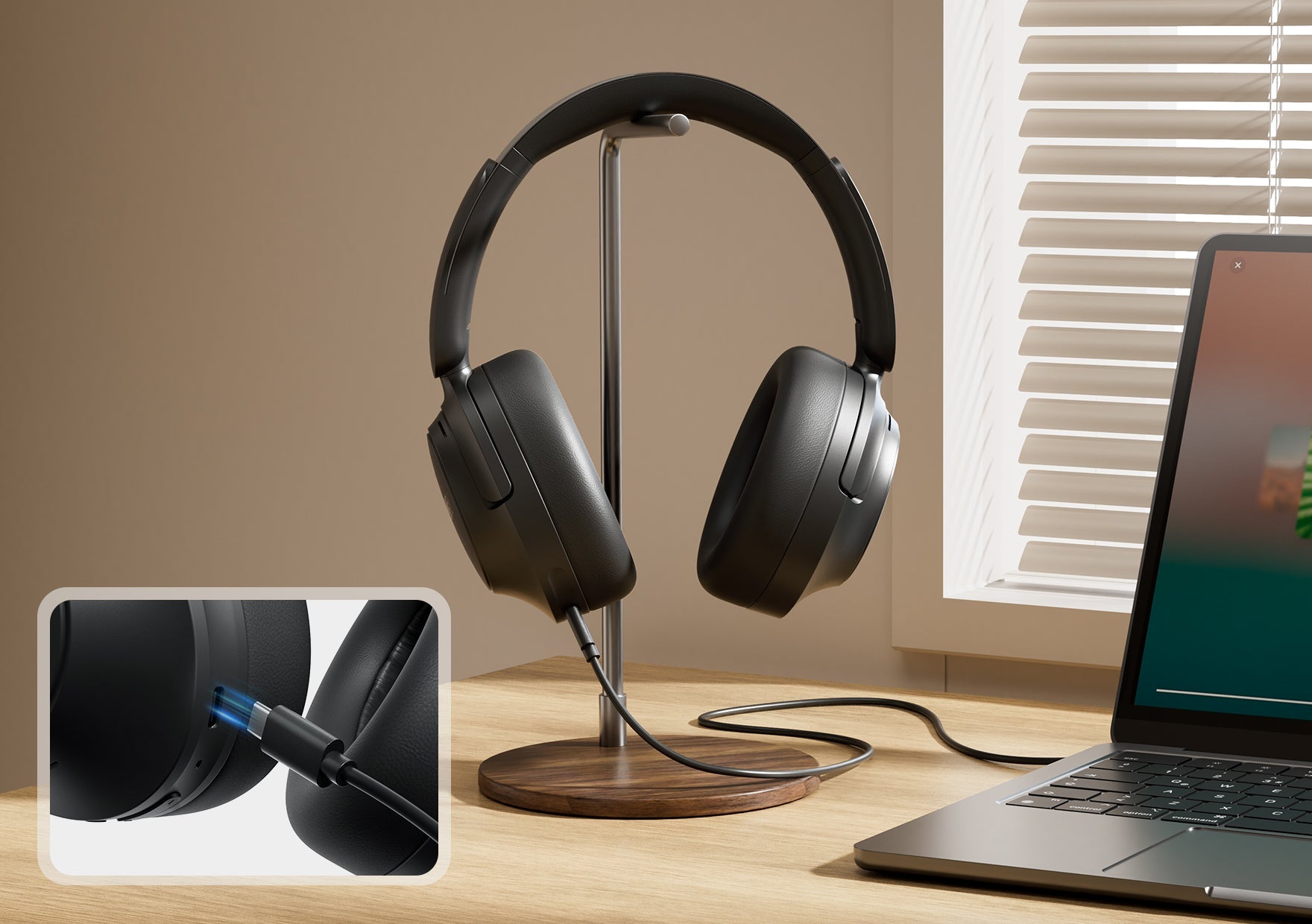 Auriculares negros circumaurales con cable sobre un soporte de madera junto a un portátil en la ventana.