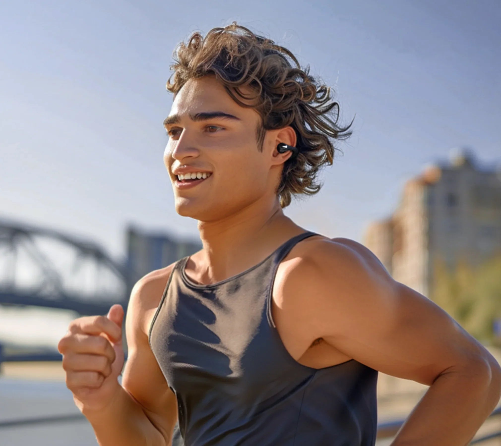Joven sonriente corriendo con auriculares inalámbricos, ropa deportiva al aire libre