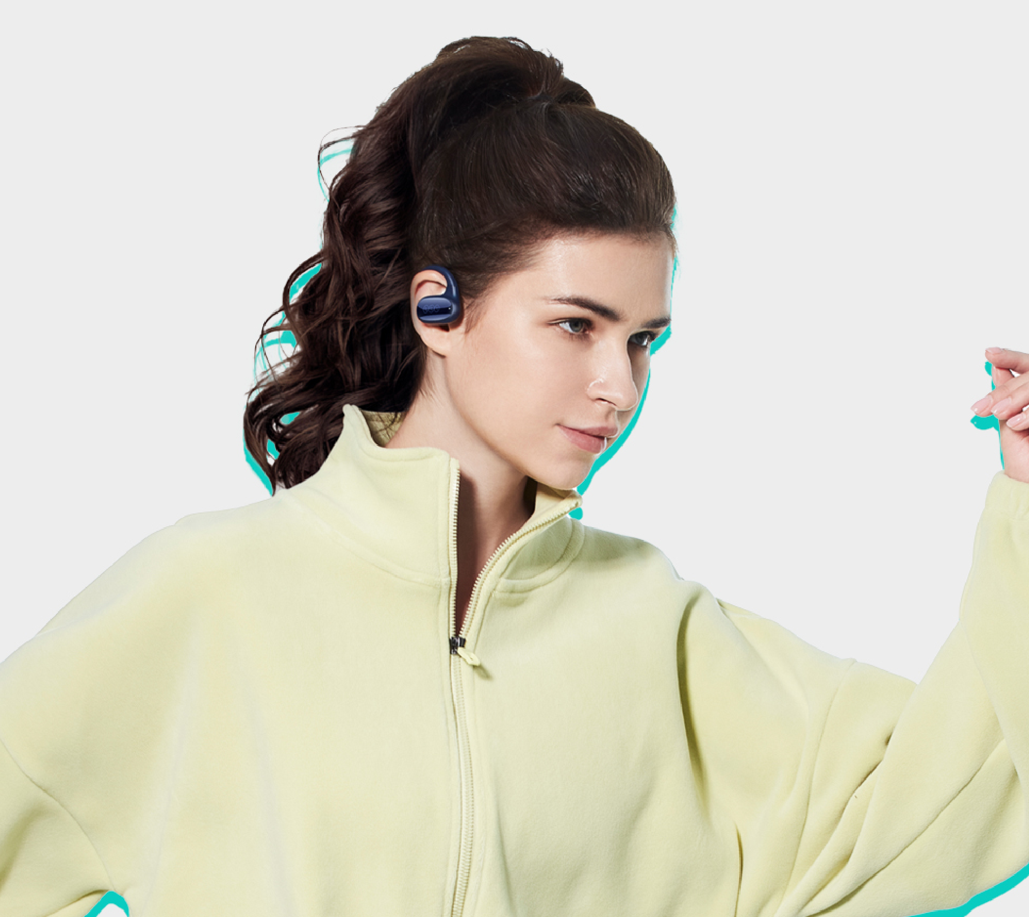 Mujer con cabello oscuro recogido en un moño, lleva auriculares deportivos azules y chaqueta de entrenamiento amarillo claro.