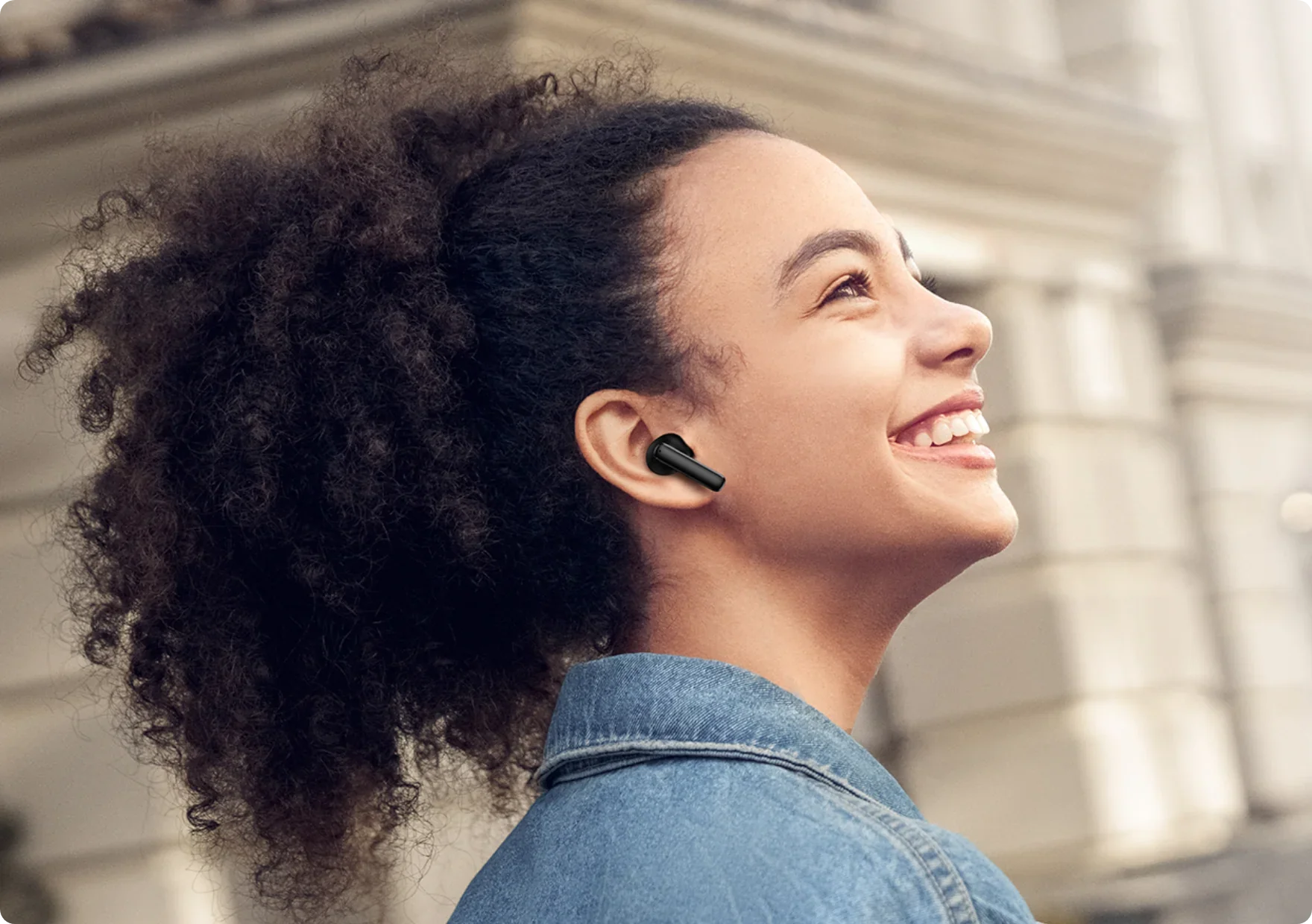 Mujer sonriente con auriculares inalámbricos negros al aire libre.