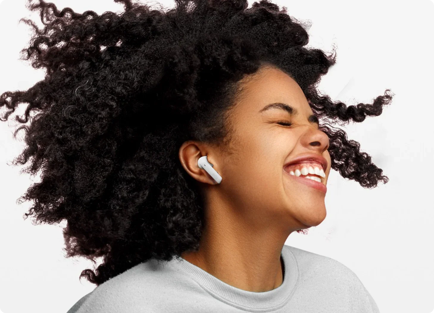 Mujer feliz con cabello rizado y auriculares intrauditivos blancos.