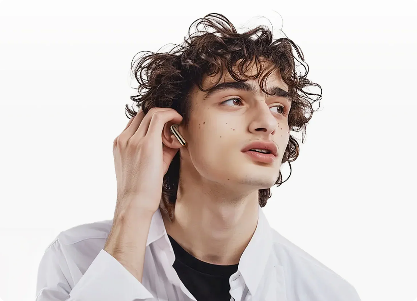 Joven con cabello rizado se pone auriculares inalámbricos dorados, camisa blanca, estilo de vida moderno.