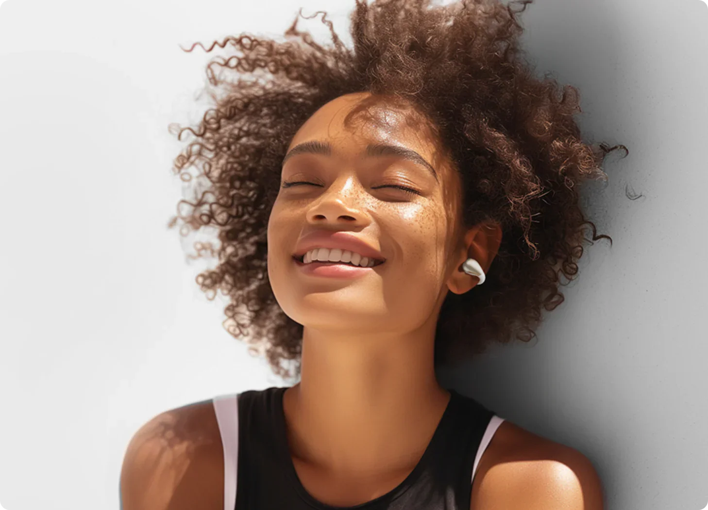 Mujer feliz con rizos y auriculares blancos disfrutando de la música.
