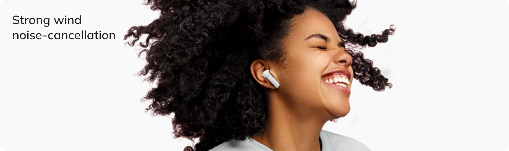 Mujer con cancelación de ruido de viento en los auriculares, sonriendo con viento fuerte.