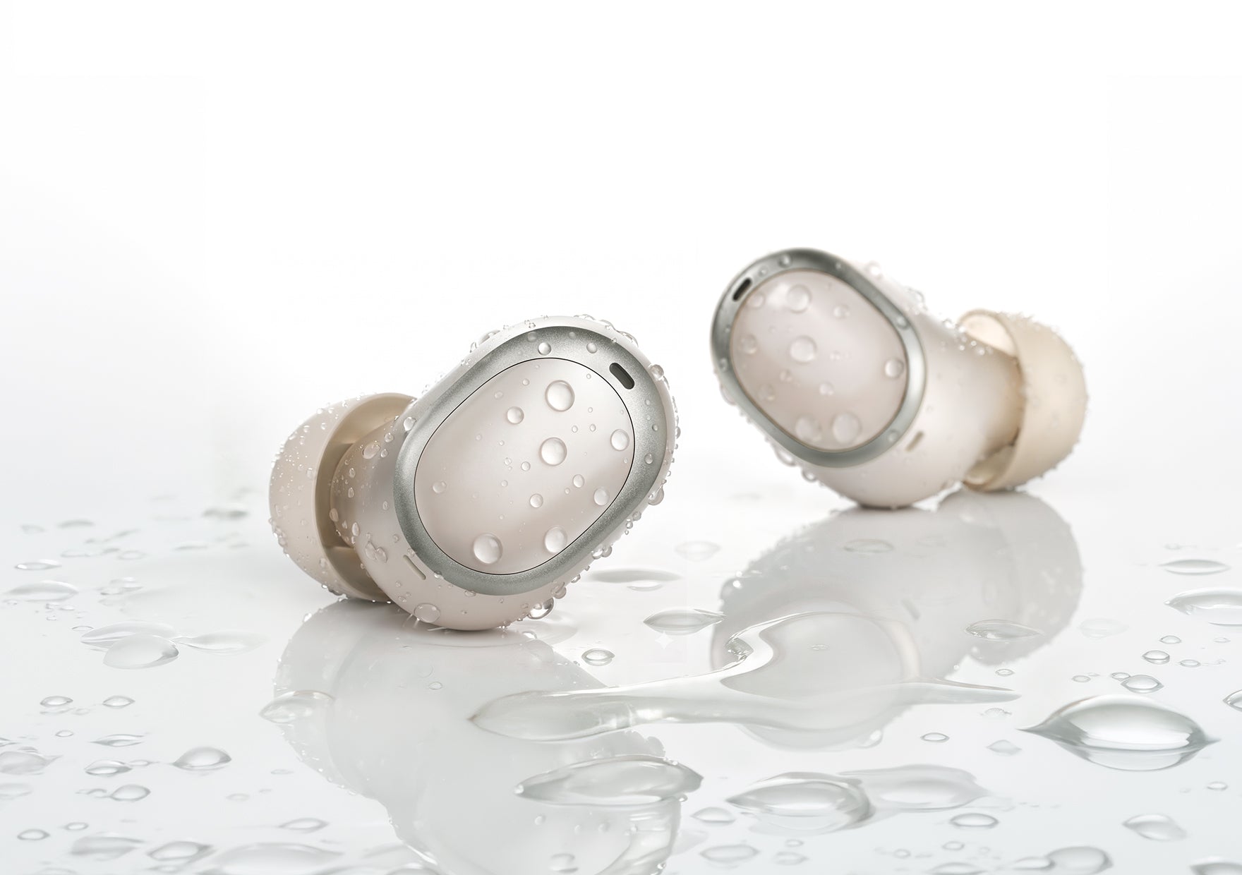 Auriculares intrauditivos blancos impermeables con gotas de agua sobre una superficie reflectante.