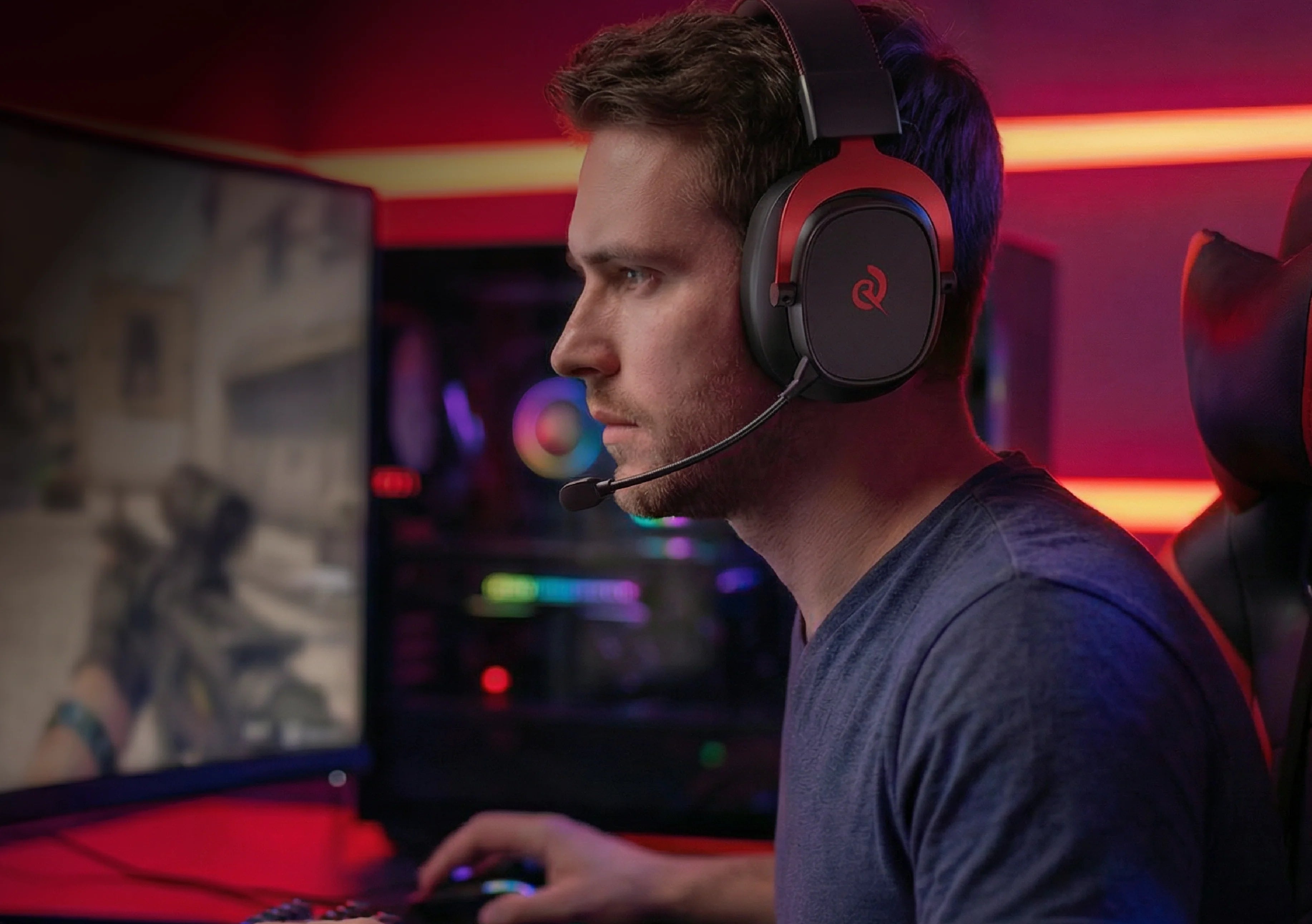 Hombre con auriculares para juegos y micrófono frente a un monitor de PC, iluminación RGB brillante de fondo